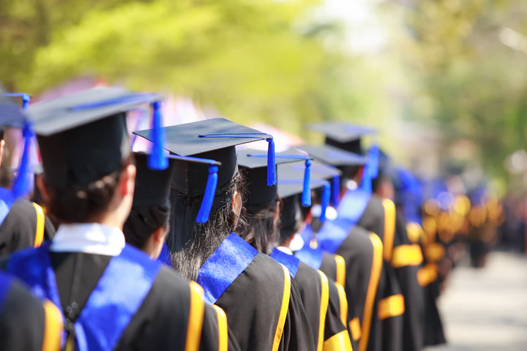 A line of students in graduation gowns and caps waiting outside