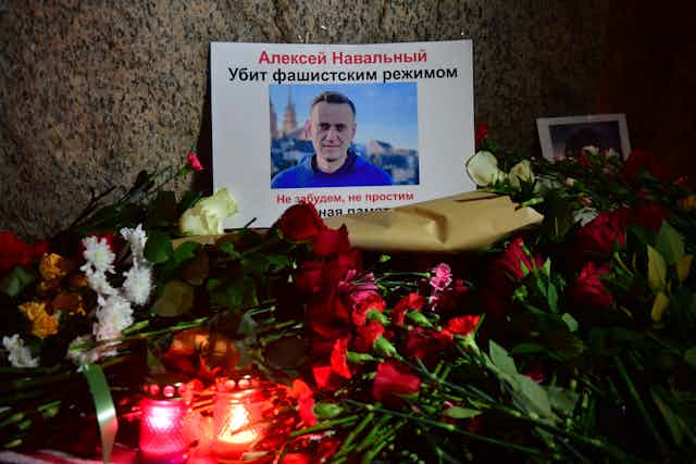 Flowers, votive candles and a photo of Alexei Navalny laid next to a large stone.