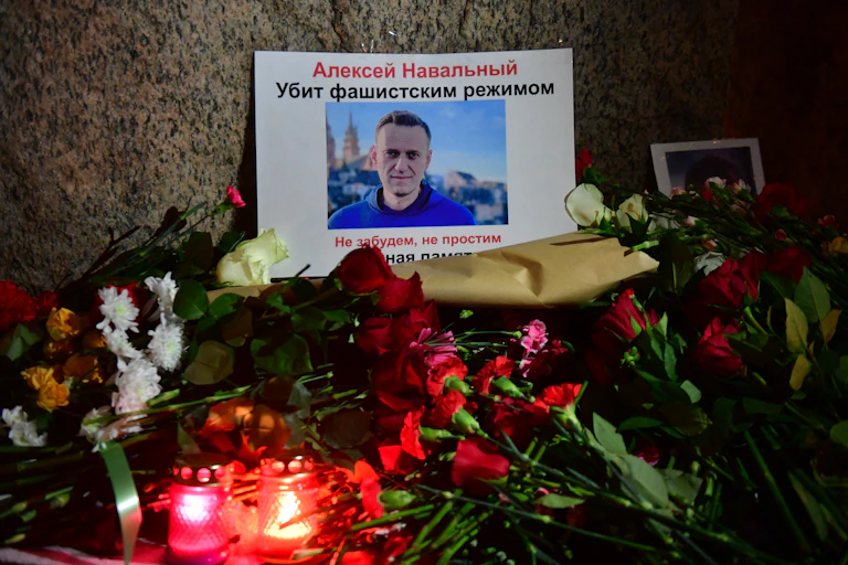 Flowers, votive candles and a photo of Alexei Navalny laid next to a large stone.