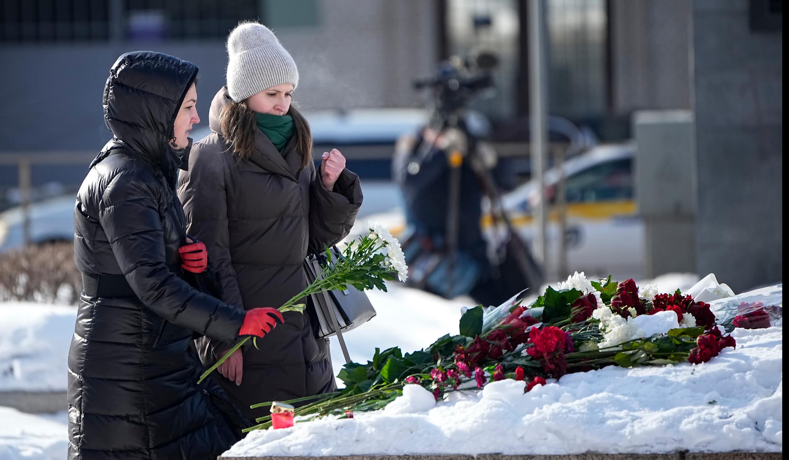 Deux femmes vêtues de longs manteaux d'hiver déposent des fleurs sur un autel de fortune enneigé, au pied d'un monument.