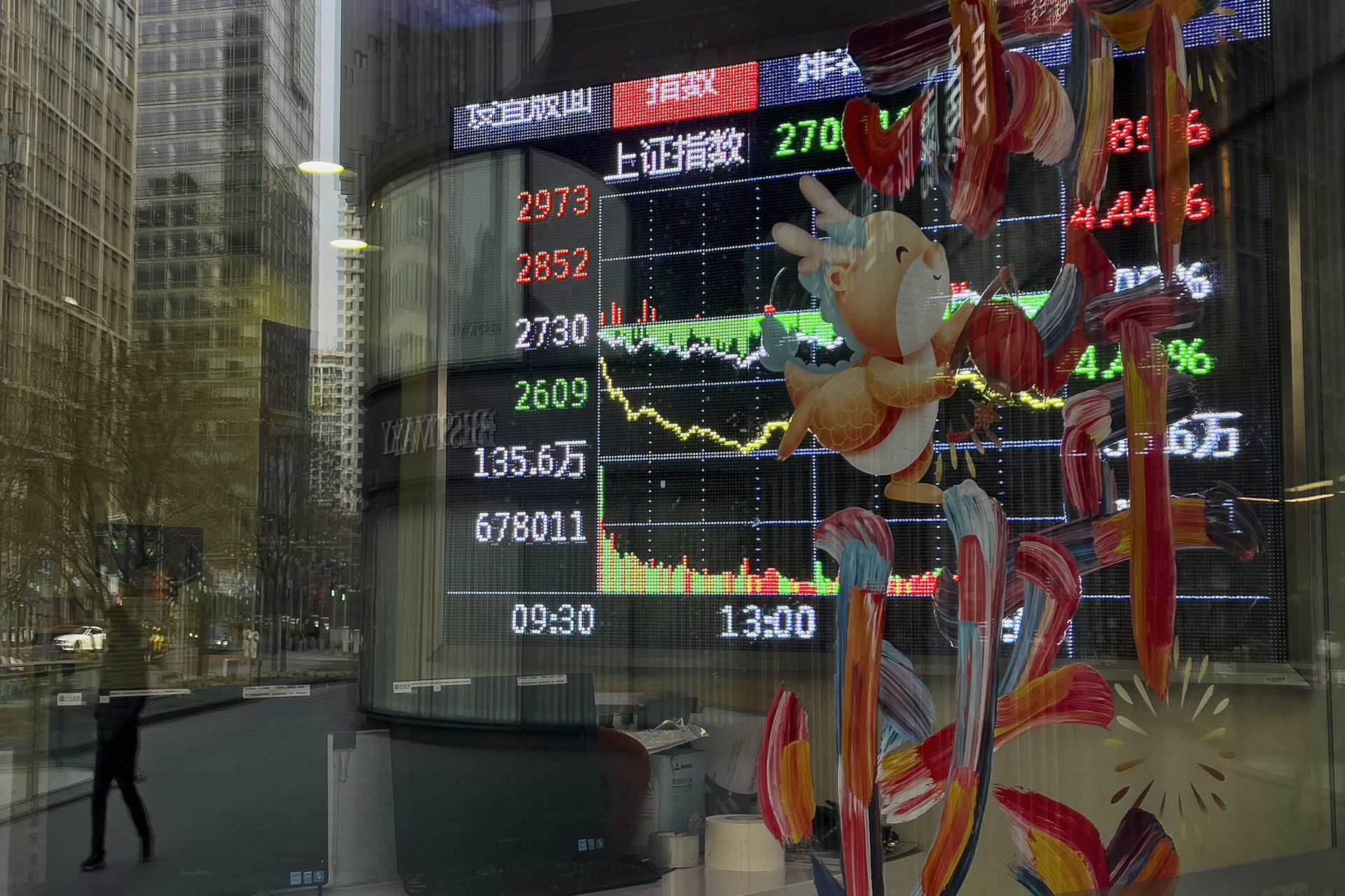 A pedestrian and office buildings are reflected on a brokerage house's window as an electronic board displaying Shanghai shares trading index