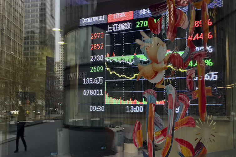 A pedestrian and office buildings are reflected on a brokerage house's window as an electronic board displaying Shanghai shares trading index