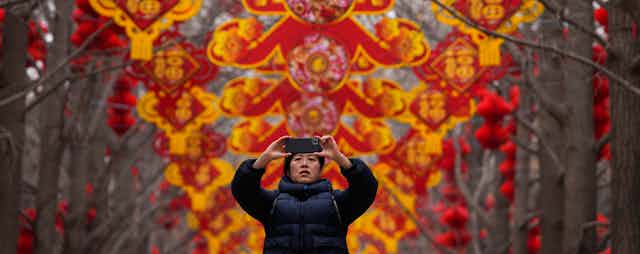 A woman takes a picture of red lanterns and decorations on display in the trees
