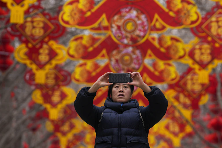 A woman takes a picture of red lanterns and decorations on display in the trees