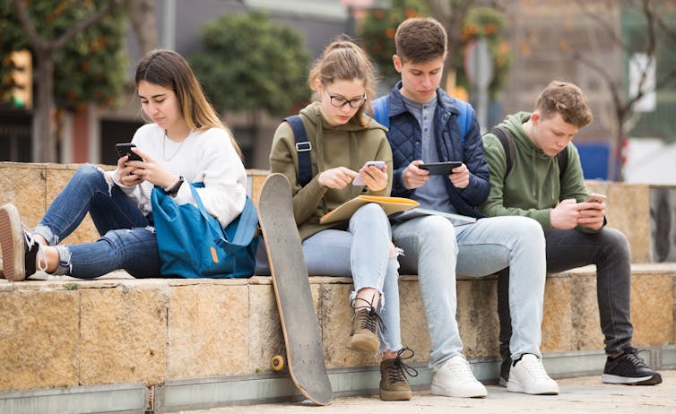 A group of teenagers sit outside and use their smartphones