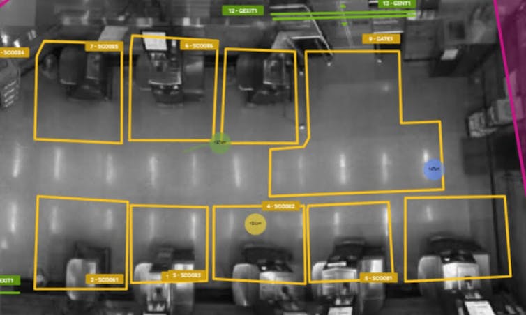 A grainy security camera image from above a self-checkout area showing areas outlined in yellow.