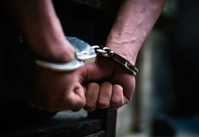 Close up photo of a man's hands in handcuffs behind his back