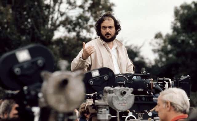 A bearded man (Stanley Kubrick) standing in front of a bank of film cameras talking to his crew.