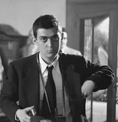 A black and white image of a dark-haired young man with a camera.