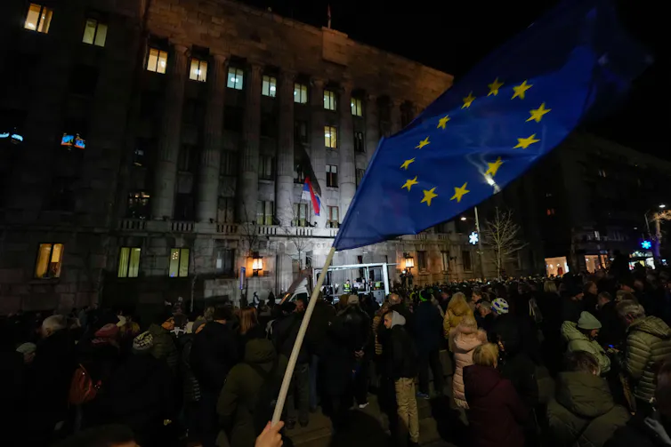 A large crowd in Serbia, one person is waving an EU flag.