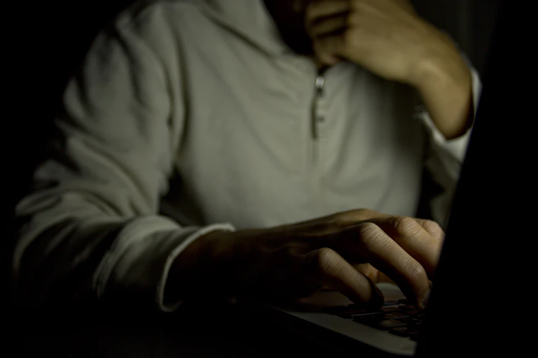 Photo of a man using a laptop in shadow, darkness