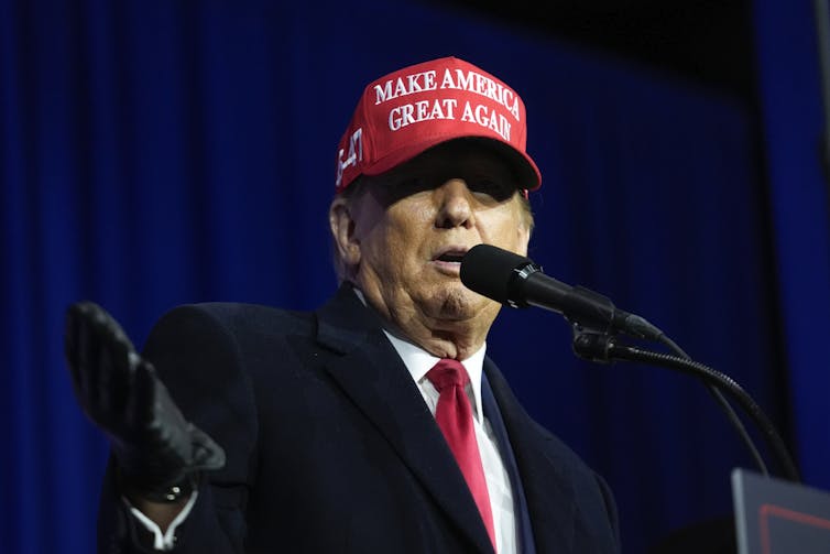 A man with an orange tinge to his skin and wearing a red ball cap that reads Make America Great Again.