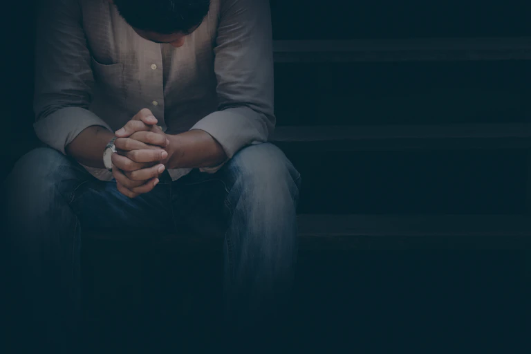 A Black man sitting on a staircase with his hands held together