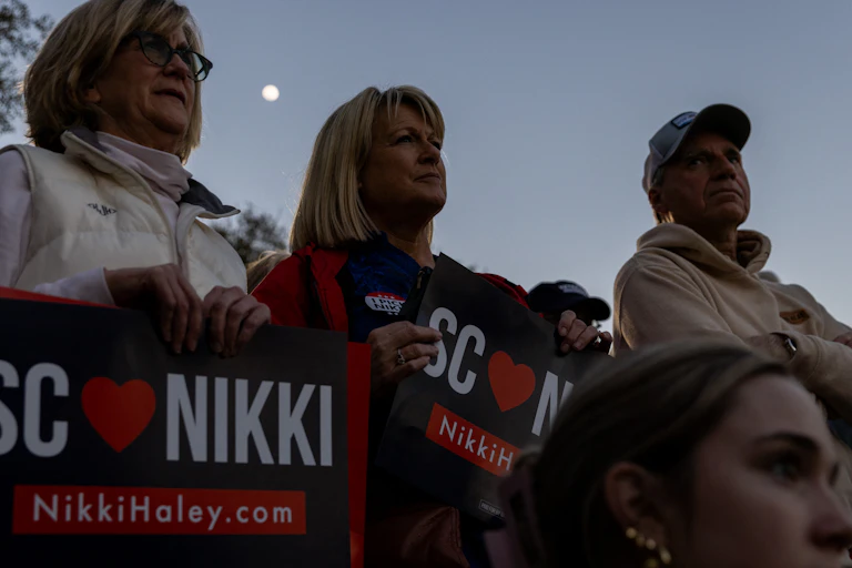Three middle aged white women look in the same direction and hold up signs that say 'SC loves Nikki'