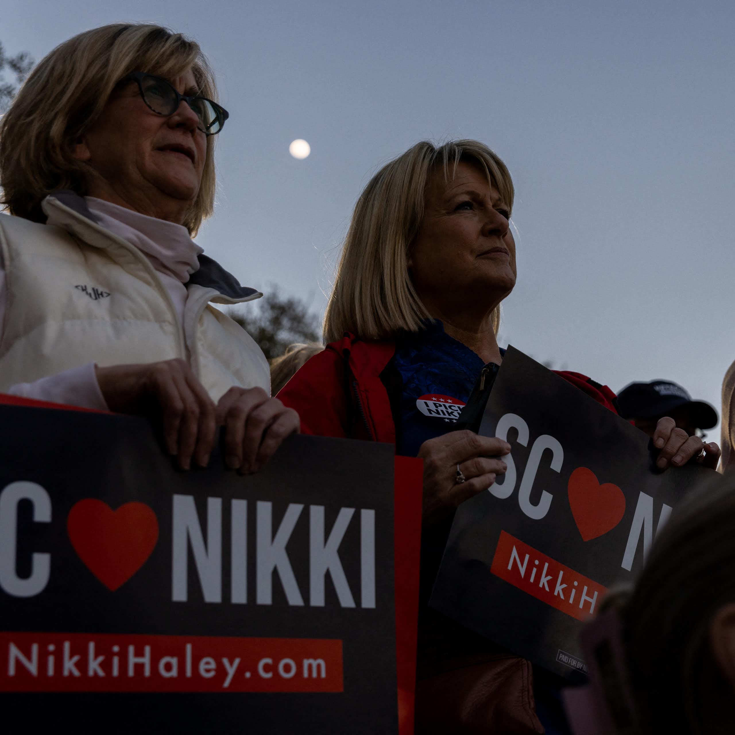 Three middle aged white women look in the same direction and hold up signs that say 'SC loves Nikki'