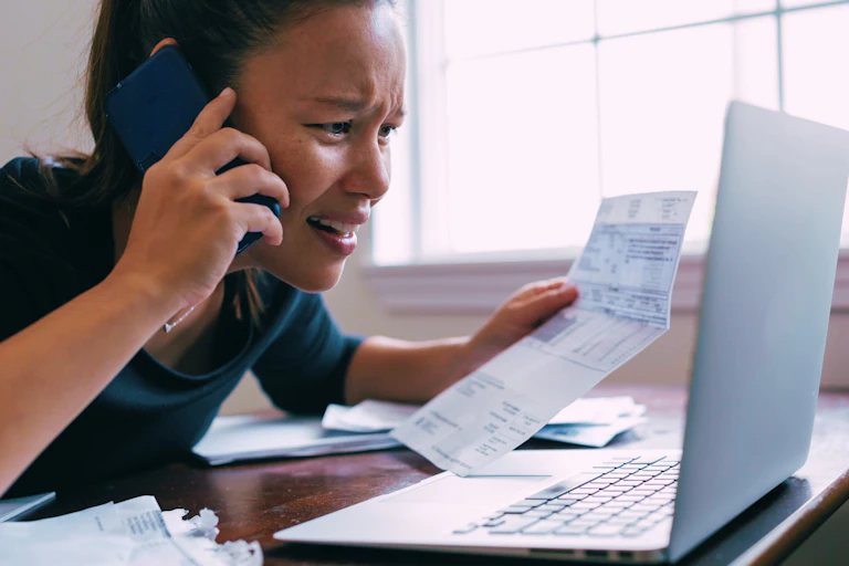 uma mulher estressada olha para o computador enquanto fala ao telefone