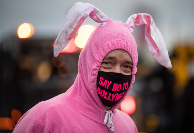 A man in a pink bunny costume wears a face mask bearing the words: say no to bullying