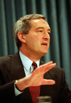A middle-aged man in a suit speaks to someone while looking off screen