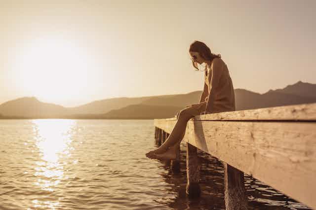 A woman sits on the edge of a pier at sunset