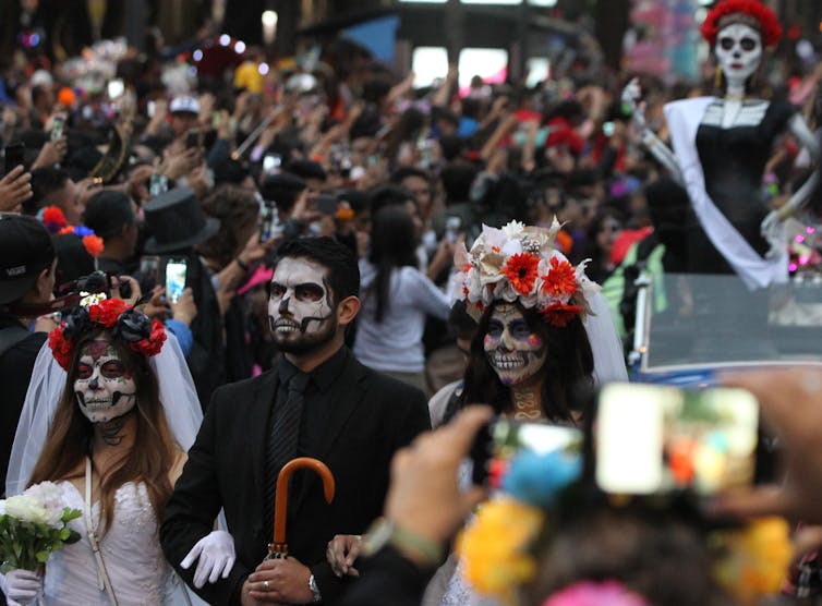 A crowd wearing skull facepaint and elaborate floral headpieces