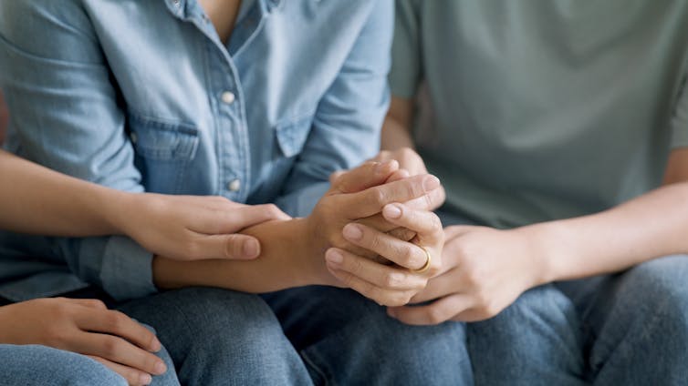 Two people hold the hands of a third person to comfort them