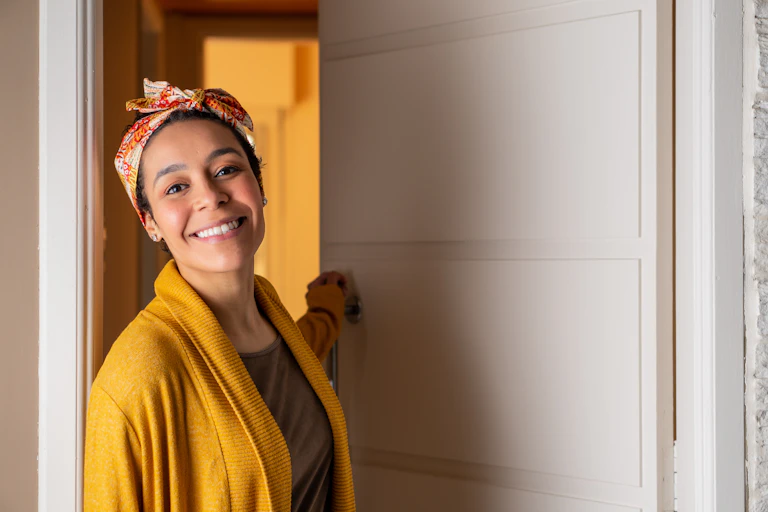A smiling woman opens the door of her apartment