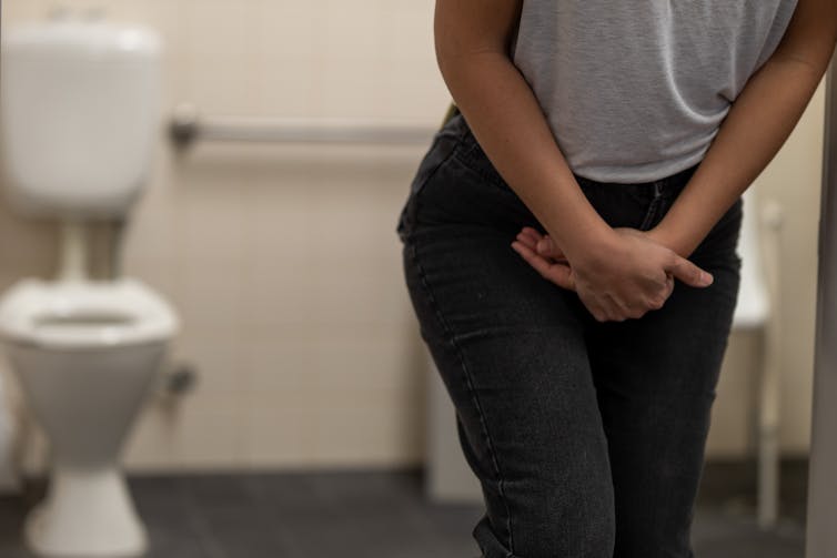 A person with their hands in front of their pelvic area in a bathroom.