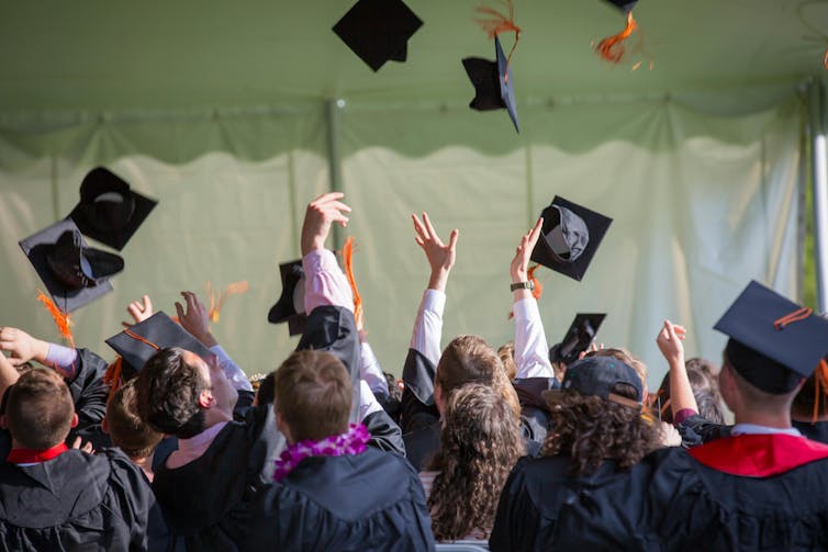 Graduating students throw their mortar boards up in the air.