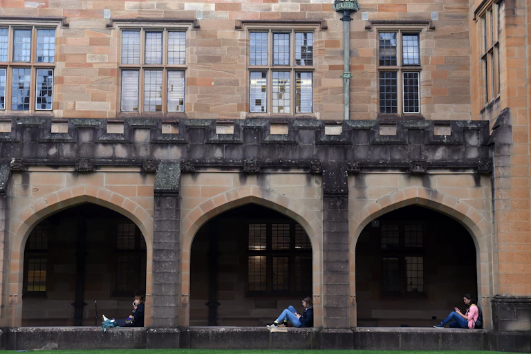 Students sit in archways in the Sydney University sandstone quadrangle.