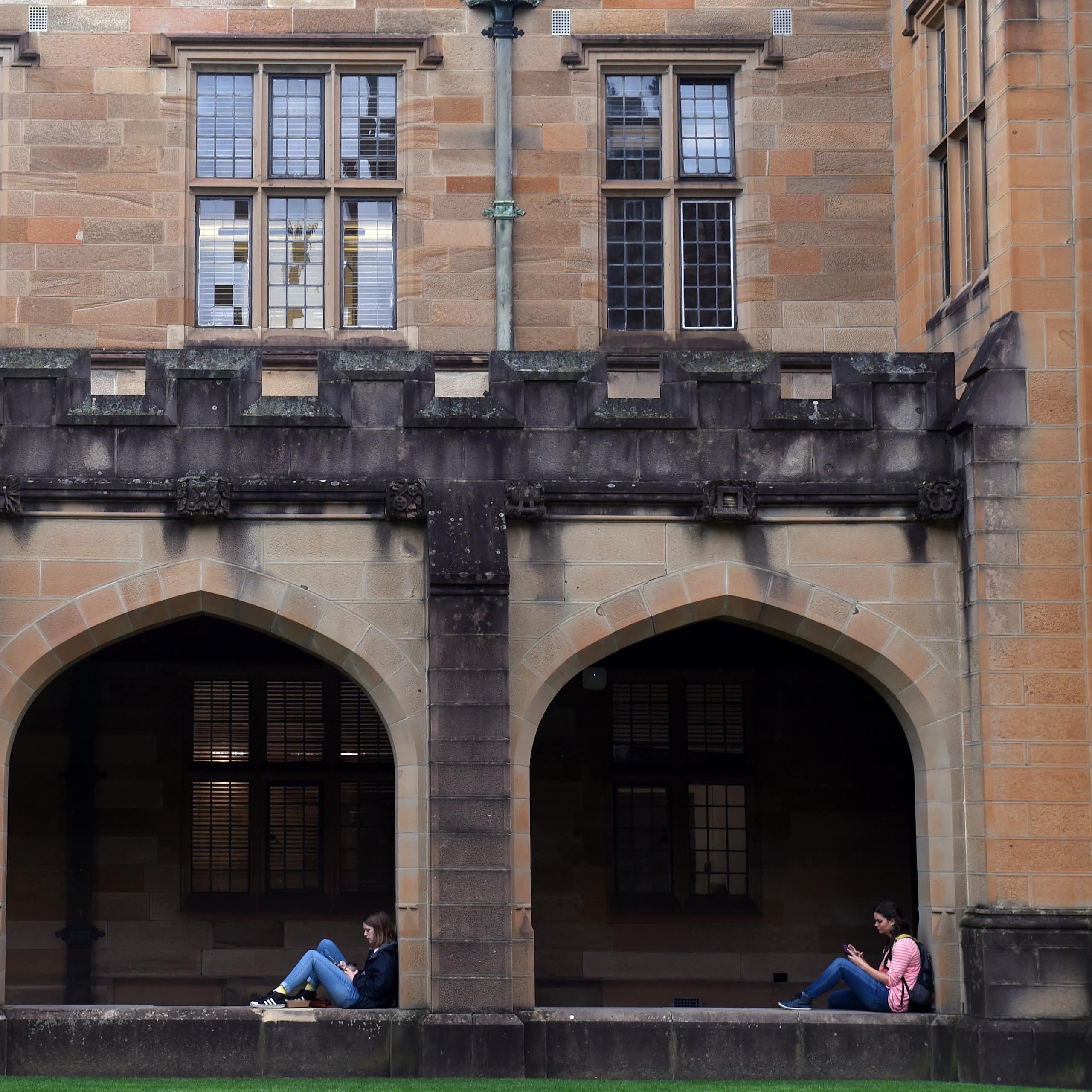 Students sit in archways in the Sydney University sandstone quadrangle. 