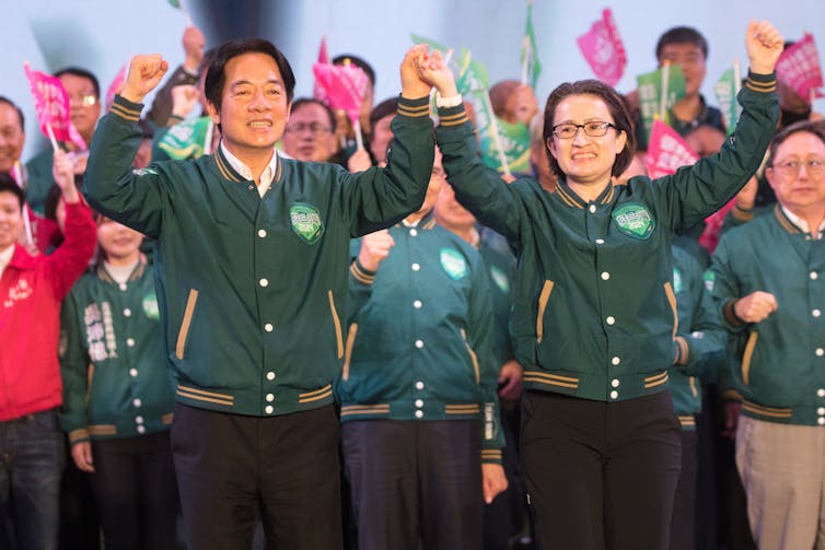 Two Taiwanese politicians (a man and a woman) cheering on a stage in front of a crowd.