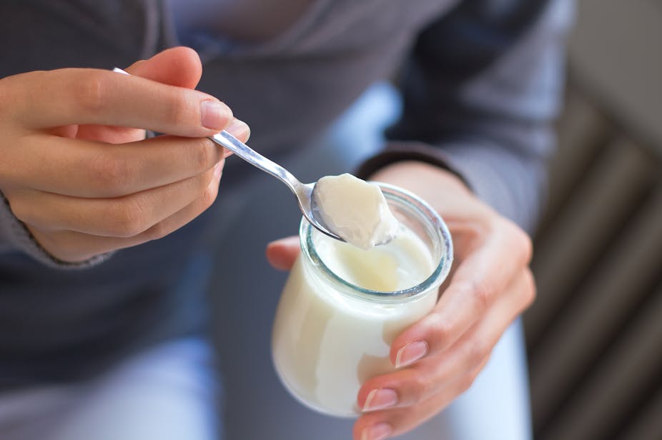 A person holds a jar and spoonful of plain yoghurt.