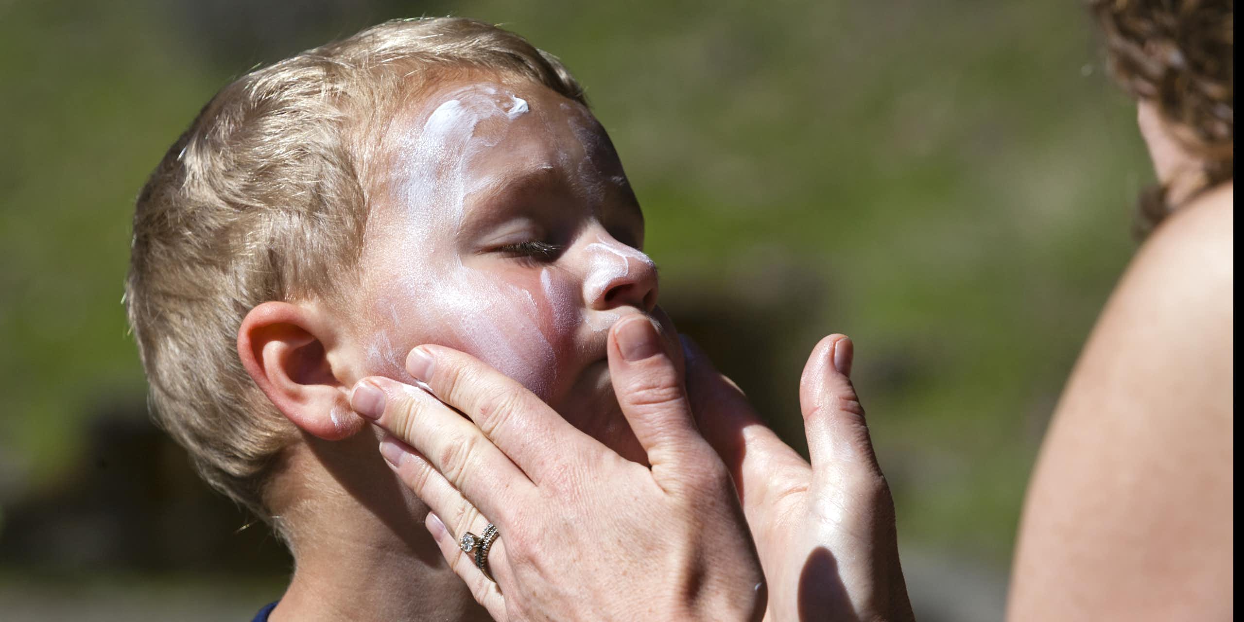 A young boy having sun cream applied to his face.