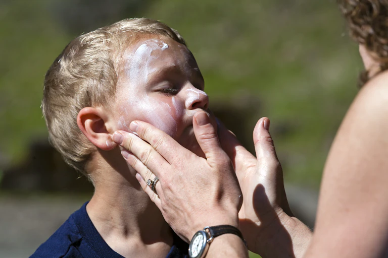 A young boy having sun cream applied to his face.