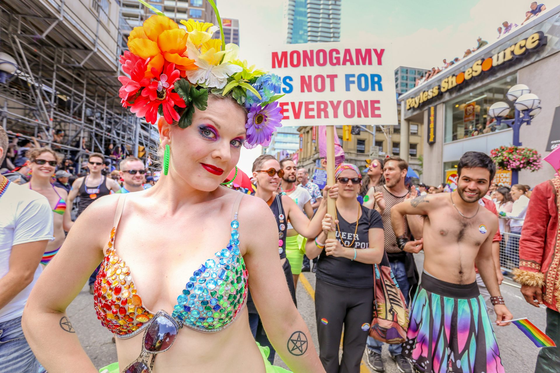 A gay mardi gras parade with a big sign saying 'Monogamy is not for everyone'.