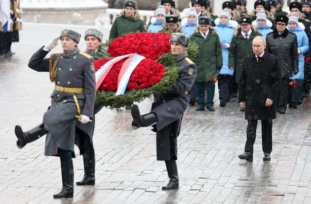 Russian president Vladimir Putin marches behind two goosestepping soldiers carrying a large wreath