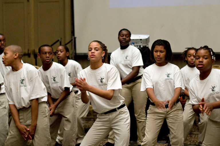 Students in white shirts and khaki pants dance and clap