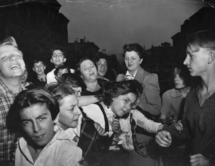 Kids tug and pull at one another while a woman cries in the background and another woman tries to keep order.