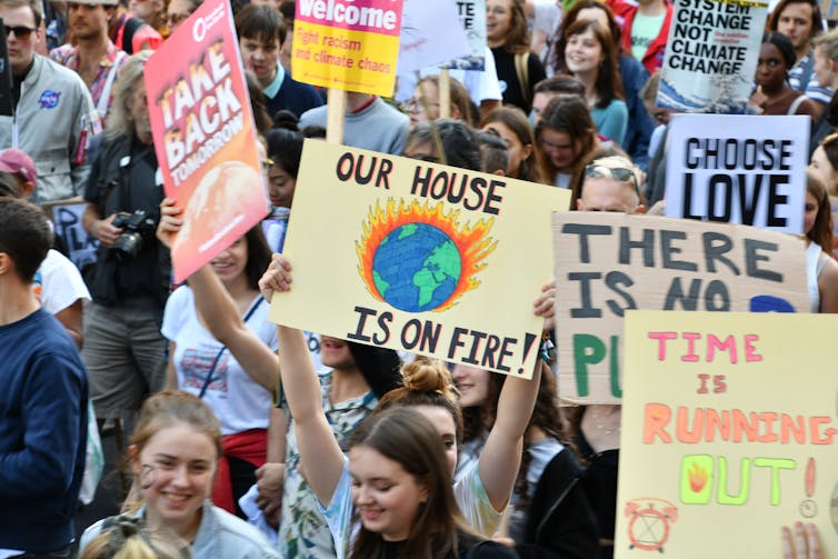 Young people carrying posters with environmental messages, including one that says 'our house is on fire' with an image of the earth burning