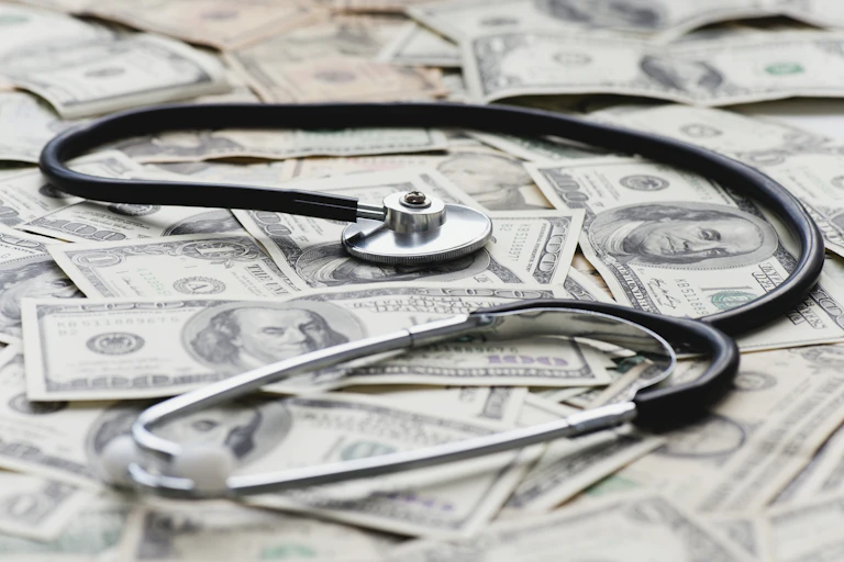 A stethoscope rests on a pile of $100 bills.