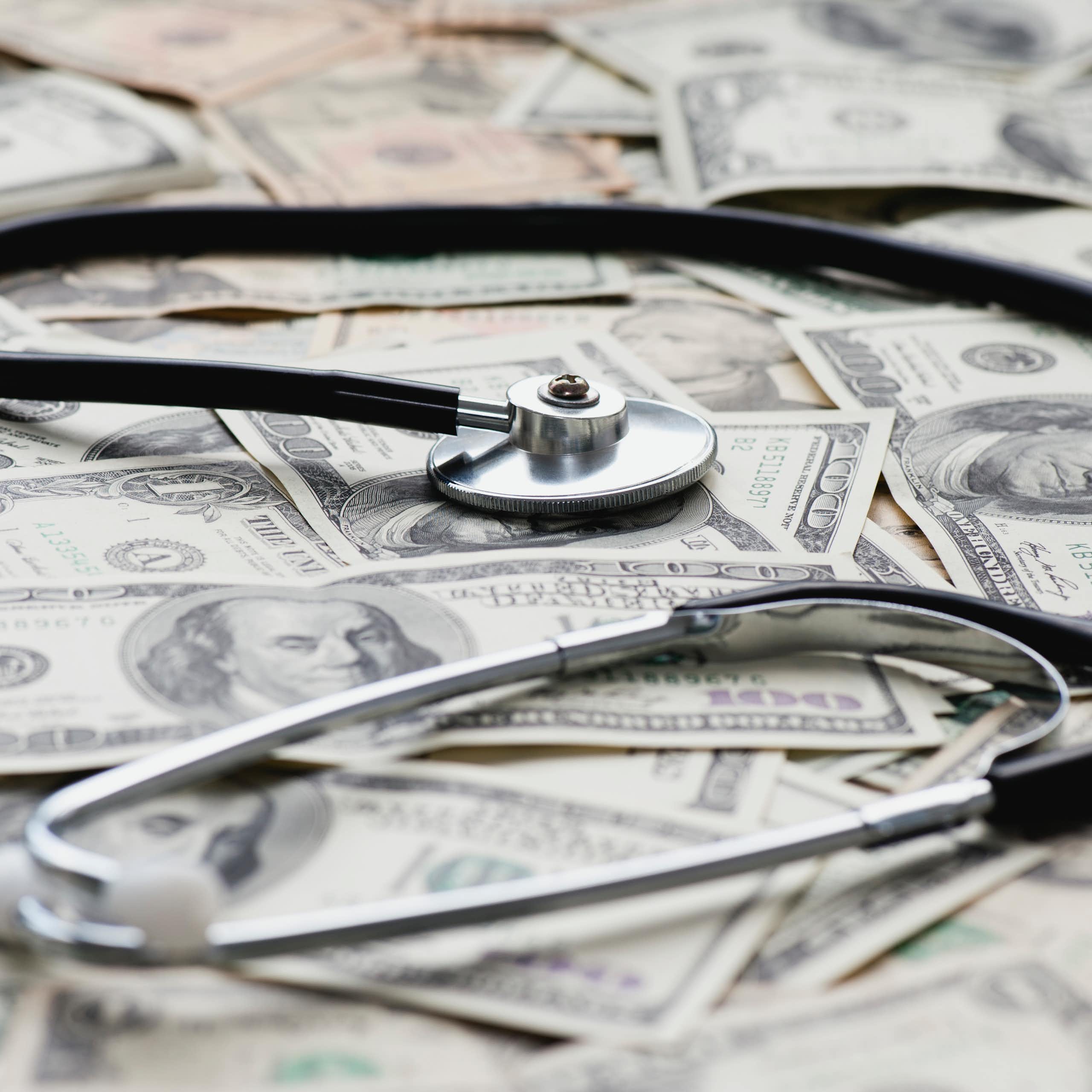 A stethoscope rests on a pile of $100 bills.