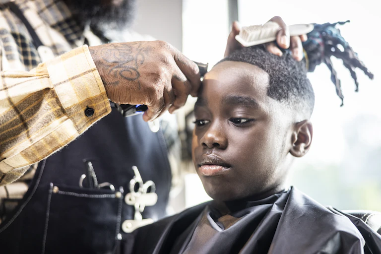 A boy with long locs is getting a haircut.