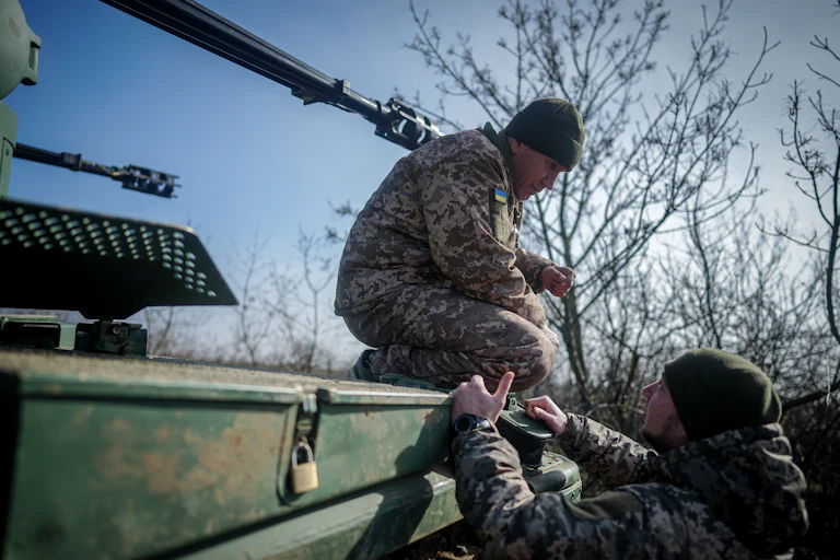 A man in army fatigues sits on a tank.