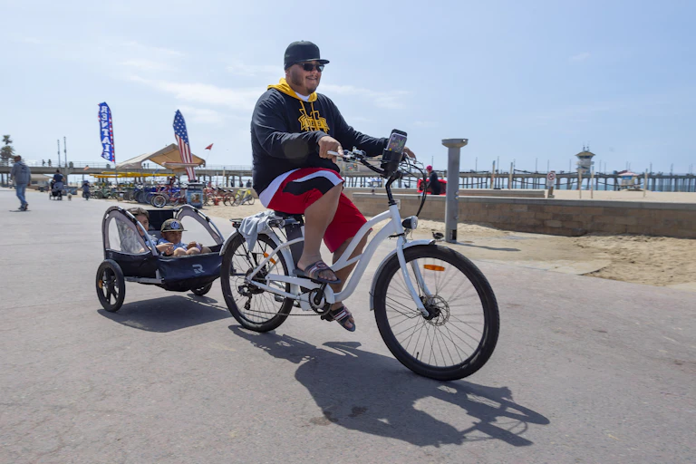 A man rides an e-bike, towing two small children in a trailer.
