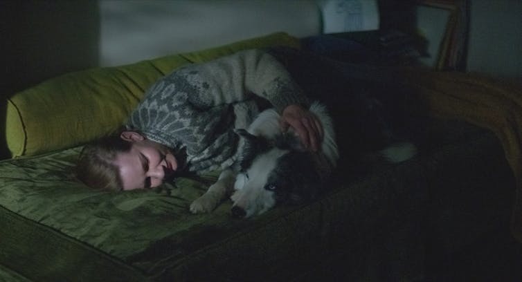 Film still: a woman lies on a bed with a dog.
