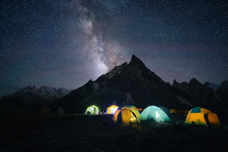 Five tents glow against the night sky with a tall mountain in the background.