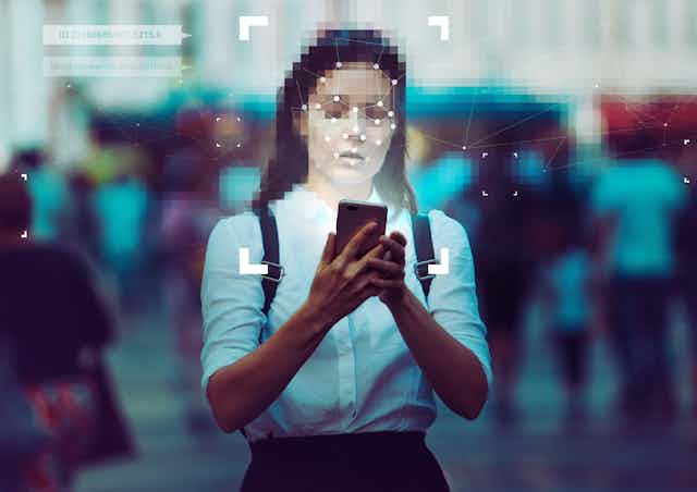 A woman with a pixelated face standing in a crowd using a smartphone