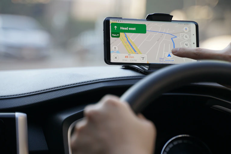 A photo of a person driving a car and looking at Google Maps on their phone.