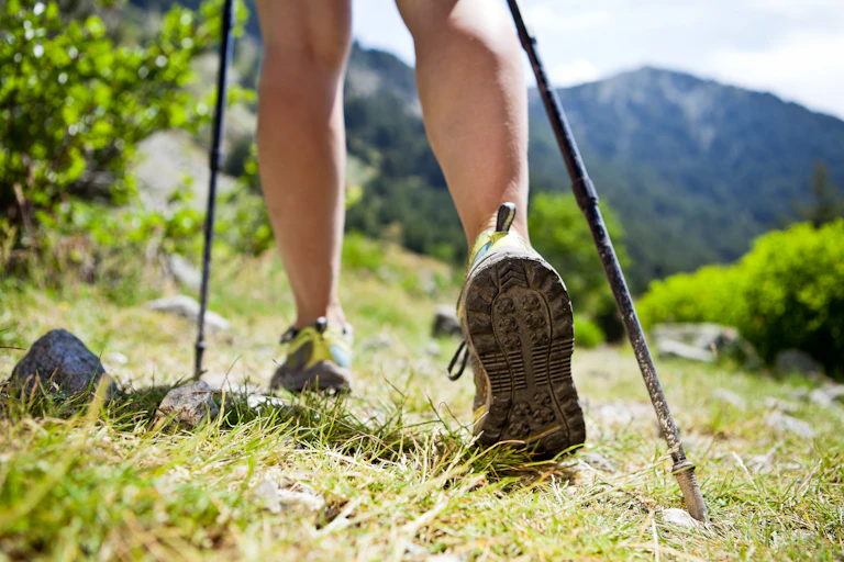 Close up of legs in trainers with walking poles going on a mountainous trek