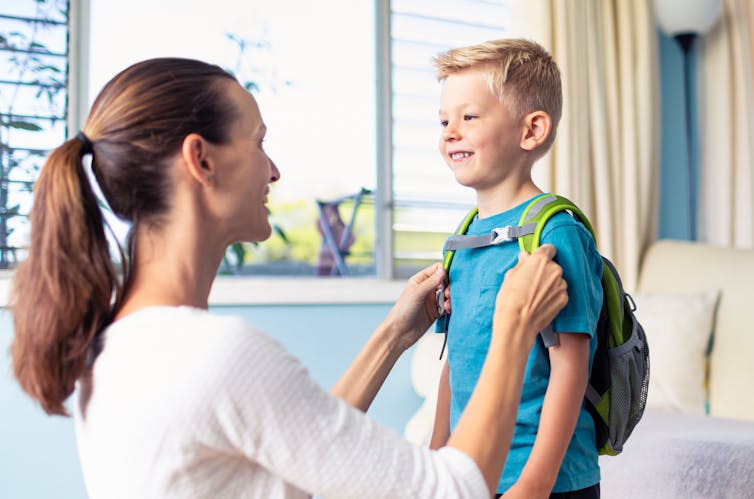 A mother getting her son ready, fastening his backpack.